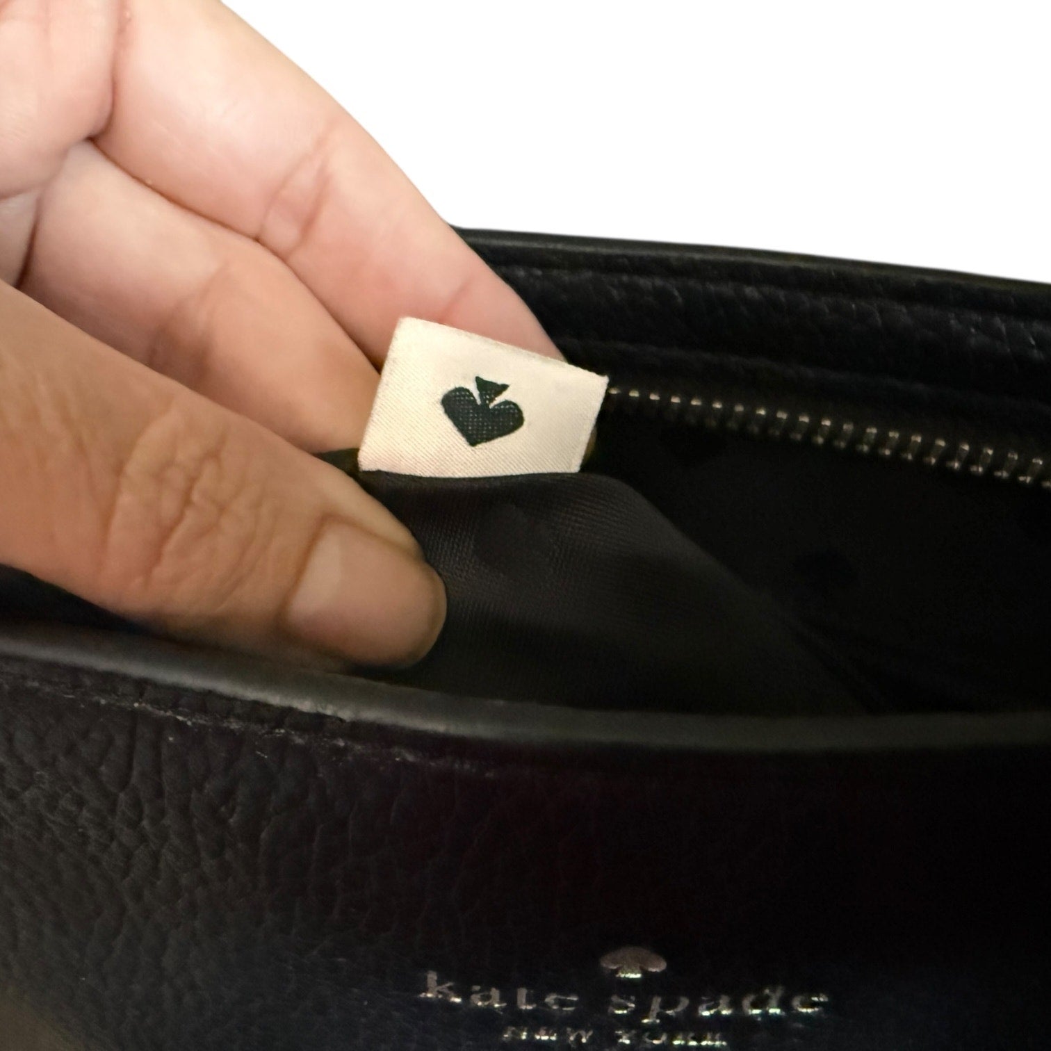 Hand holding a black Kate Spade purse with a visible brand label.