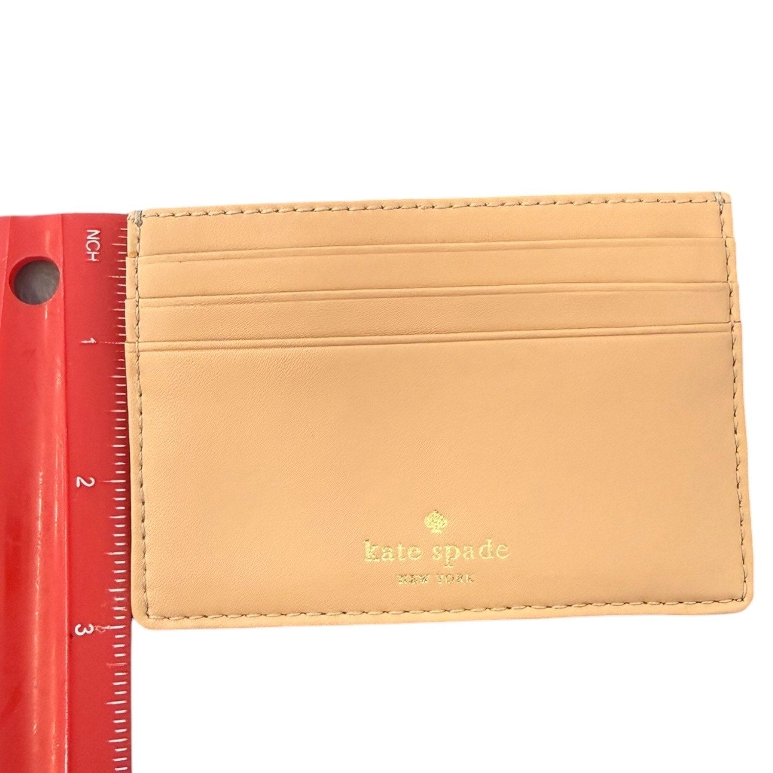 Cardholder with 'kate spade' logo next to a red ruler on a white background