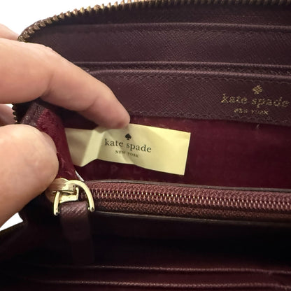 Close-up of a maroon Kate Spade wallet with a hand holding it open.