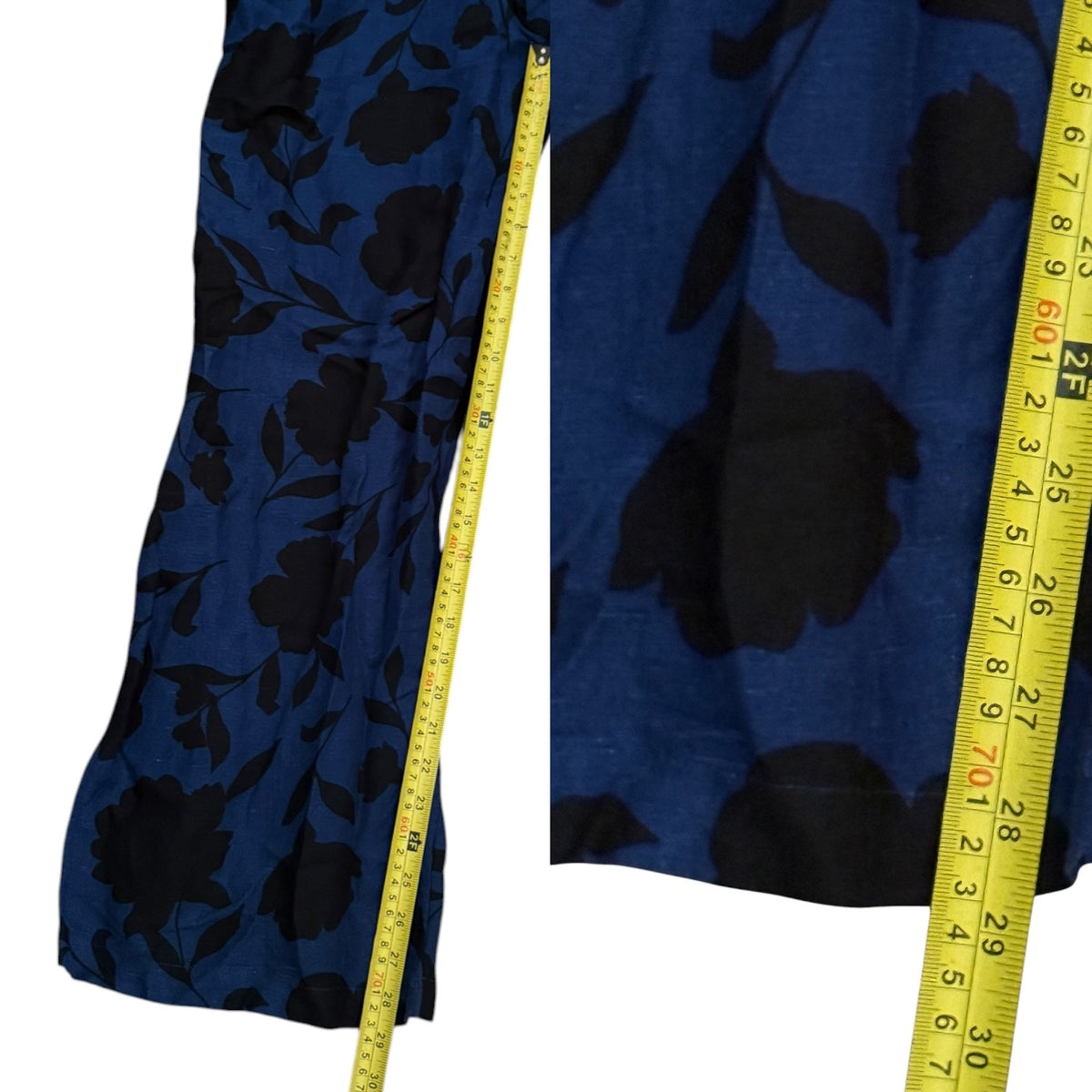 A close-up of a blue jumpsuit with a large black floral print, shown next to a yellow measuring tape to indicate size.