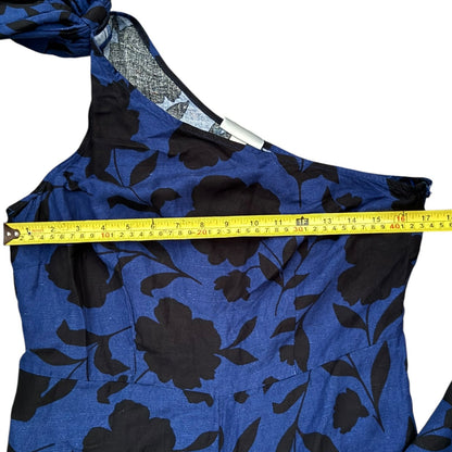 A close-up of a blue and black floral print garment with a measuring tape laid horizontally across the chest to show the width.