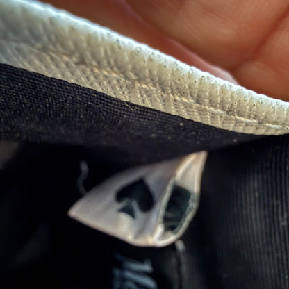 Close-up of interior of card wallet held open by a hand, showing a white stitched edge and a small sewn-on label with a black spade symbol.