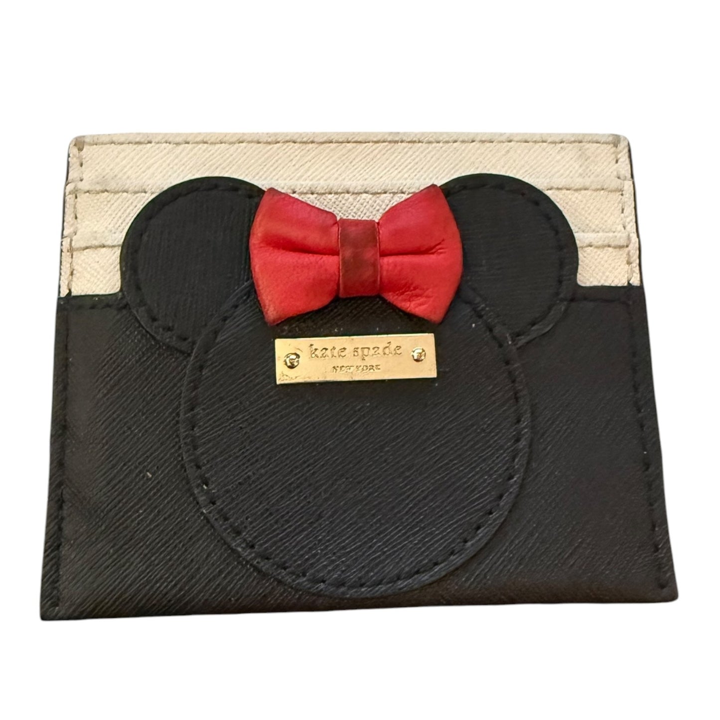 A Kate Spade New York card holder featuring a black Minnie Mouse silhouette with a red bow tie and a gold-tone brand plaque, set against a cream canvas background.