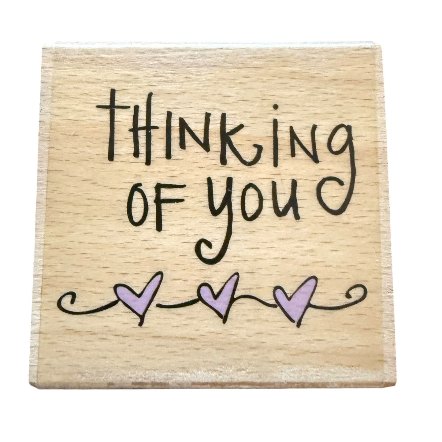 A square wooden block with the words 'THINKING OF YOU' in black , decorated with three small lavender hearts and black swirl lines underneath, shown on a plain white background.
