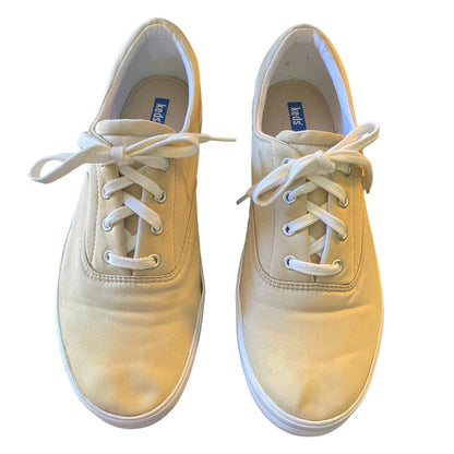 A pair of canvas low-top sneakers in a beige color with white laces, shown from a top-down view on a white background.