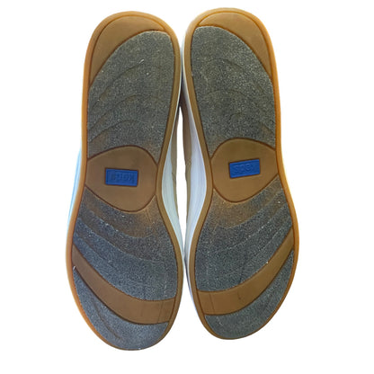 Top-down view of a pair of shoes showing the outsoles, featuring a textured gray and brown tread pattern with a blue brand patch in the center of each sole.