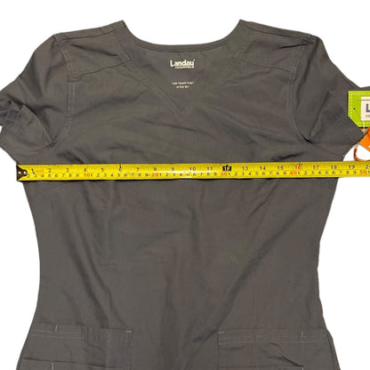 A dark gray scrub top with a yellow tape measure stretched horizontally across the chest to show the width, on a white background.