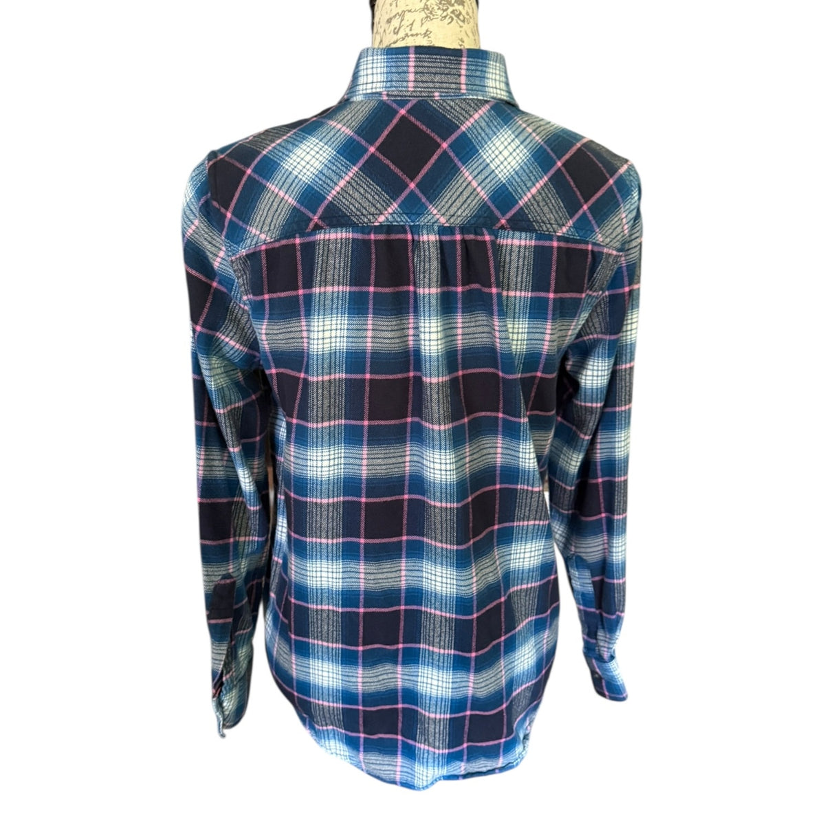 A long-sleeve plaid button-down shirt displayed on a mannequin torso, showing the back view. The shirt features a blue, black, and white plaid pattern with thin pink accent lines.