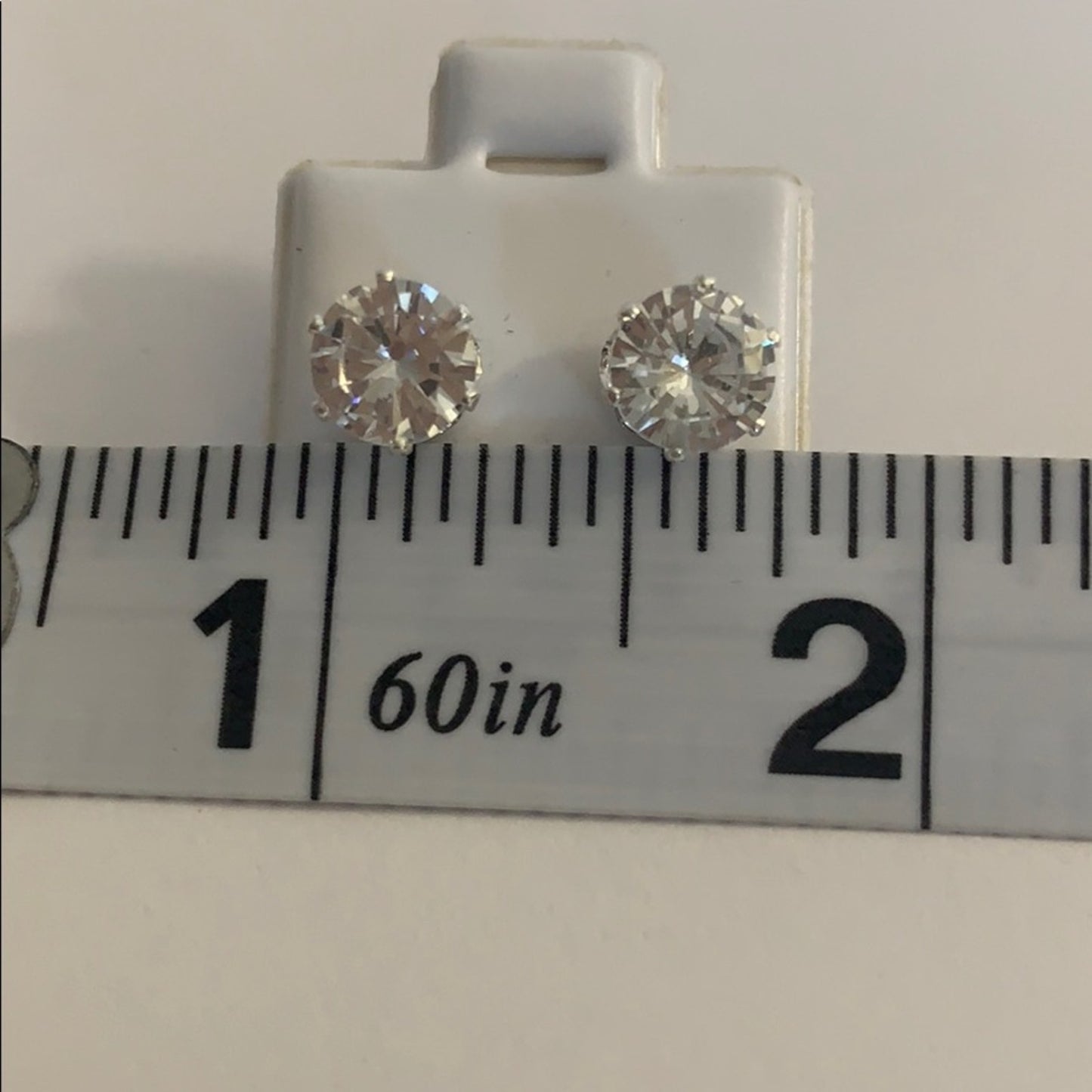 Pair of silver stud earrings on a white card with a ruler for scale.
