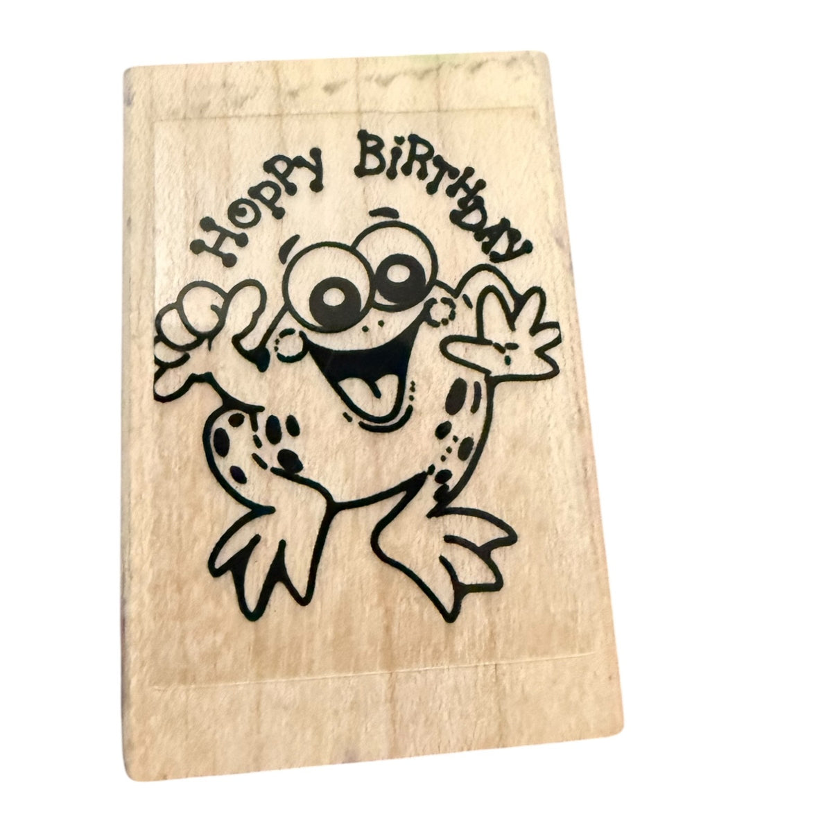 Wooden stamp with a cartoon frog and 'Hoppy Birthday' text on a white background