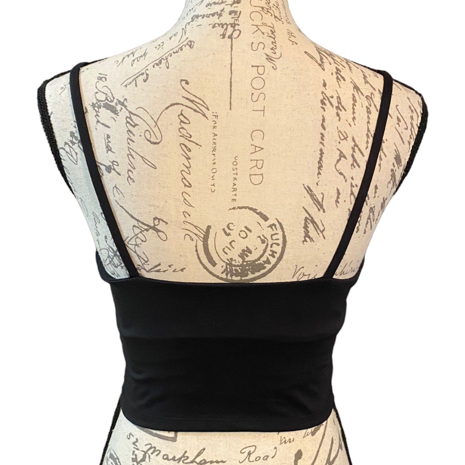 Back of Black tank bra with thin straps on a mannequin with a vintage-style script background