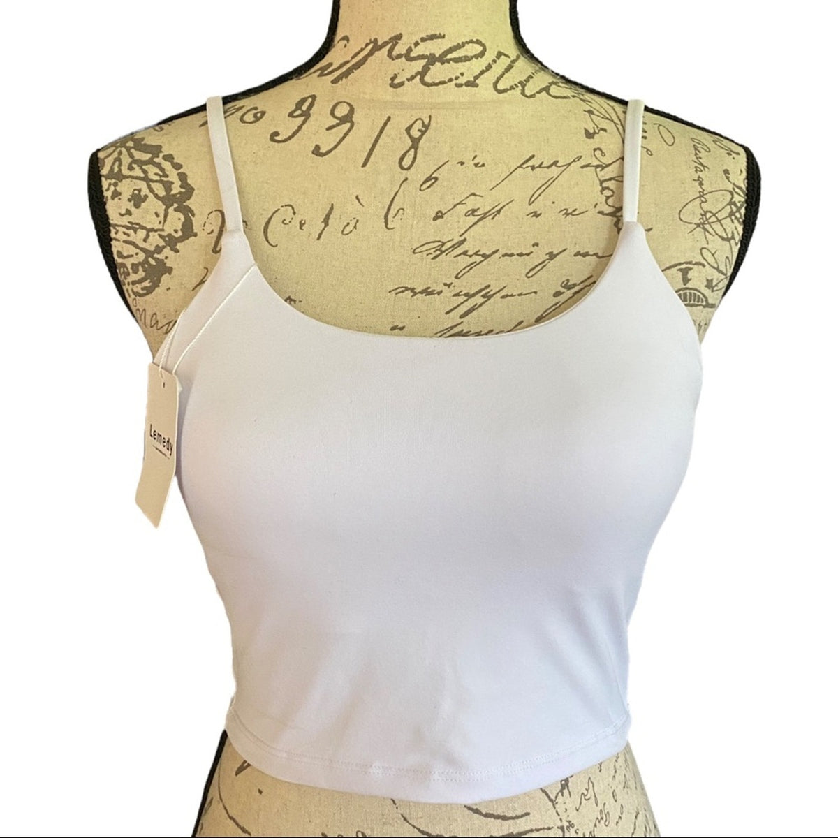 A white spaghetti-strap tank workout top displayed on a vintage-style patterned dress form mannequin against a plain white background.