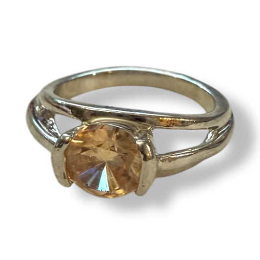 A silver-toned ring featuring a round, faceted orange-colored gemstone in a prong setting, shown against a plain white background with a soft shadow.