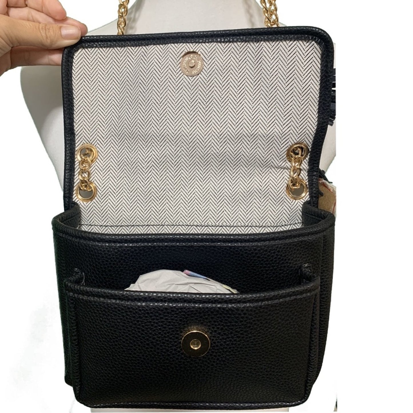 Black handbag held open with gold accents held by a hand on a white background