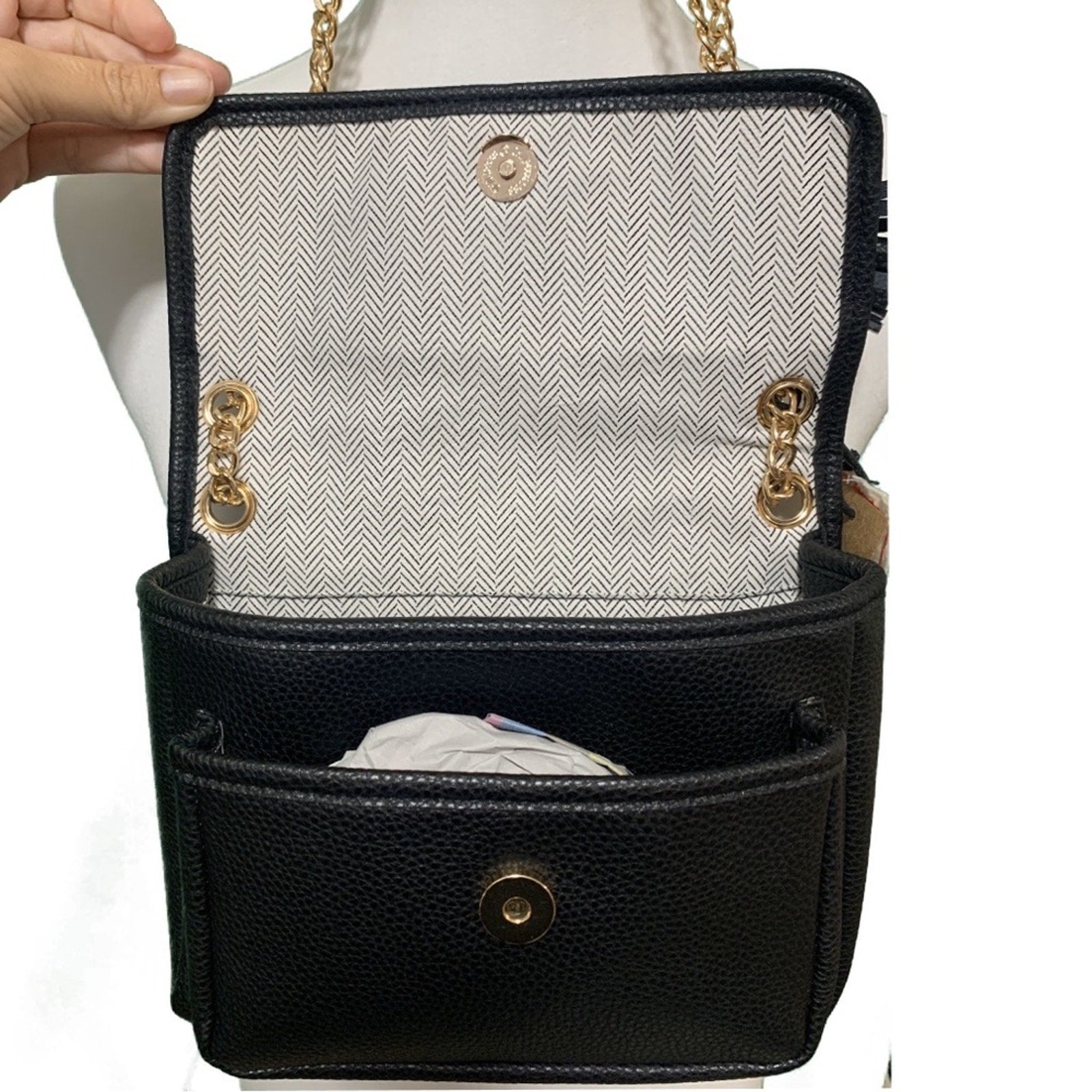Black handbag held open with gold accents held by a hand on a white background