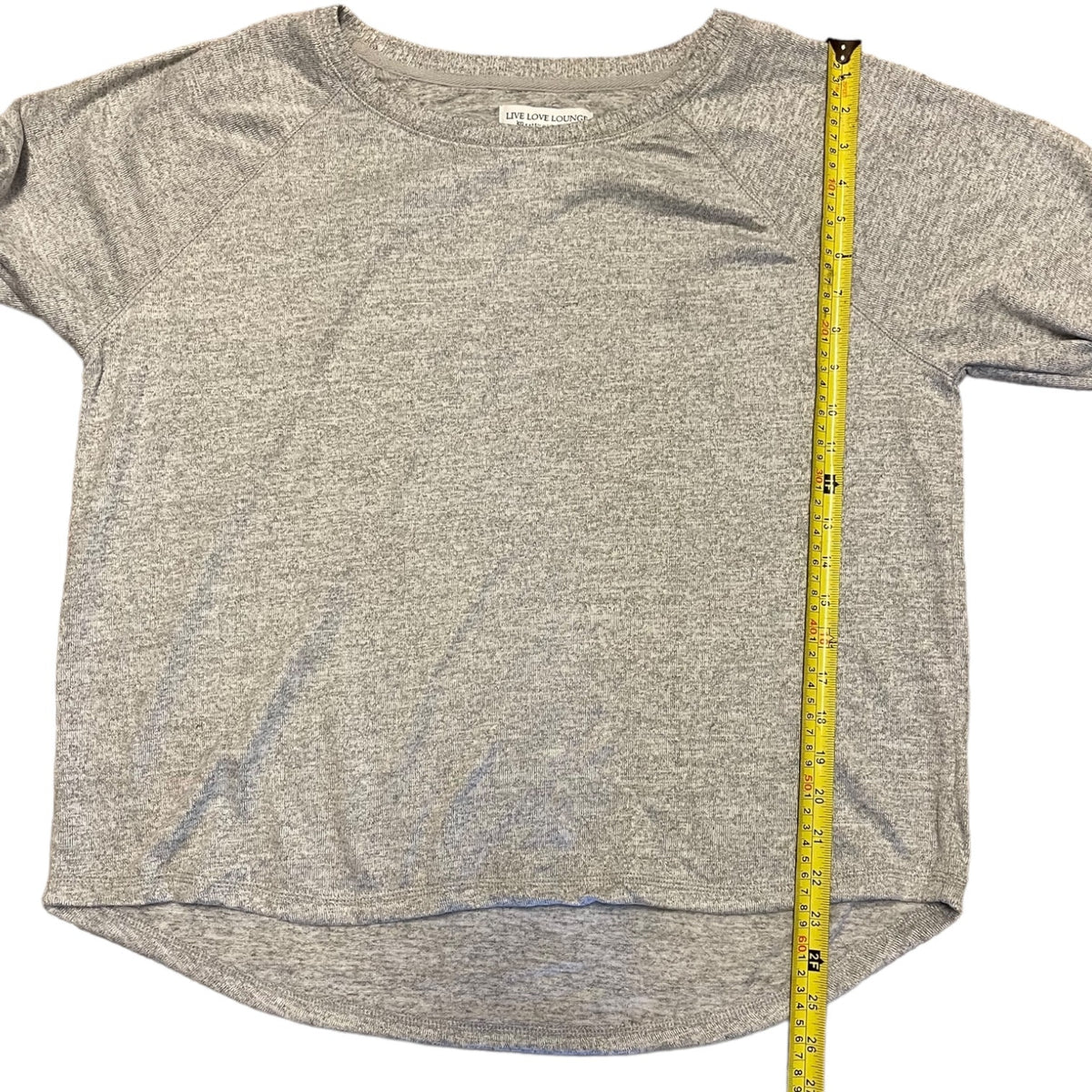 A heather gray short-sleeve crewneck shirt laid flat on a white background, with a yellow measuring tape standing vertically along the right side to show the garment's dimensions.