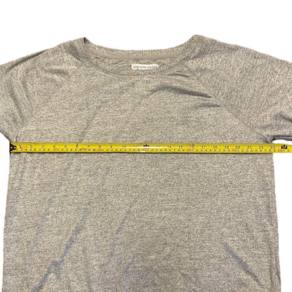 A heather gray shirt laid flat on a white background, with a yellow tape measure stretched horizontally across the chest to show the width.