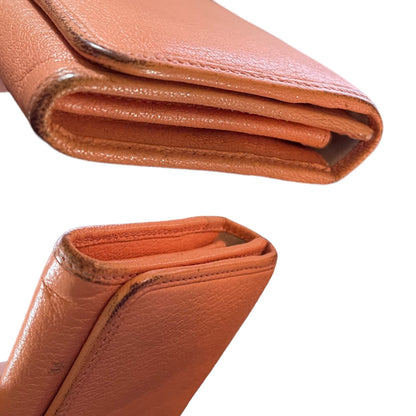 Close-up of a folded orange leather wallet shown from two angles against a white background, highlighting the pebbled leather texture and stitched edges showing scuffs on edges. 