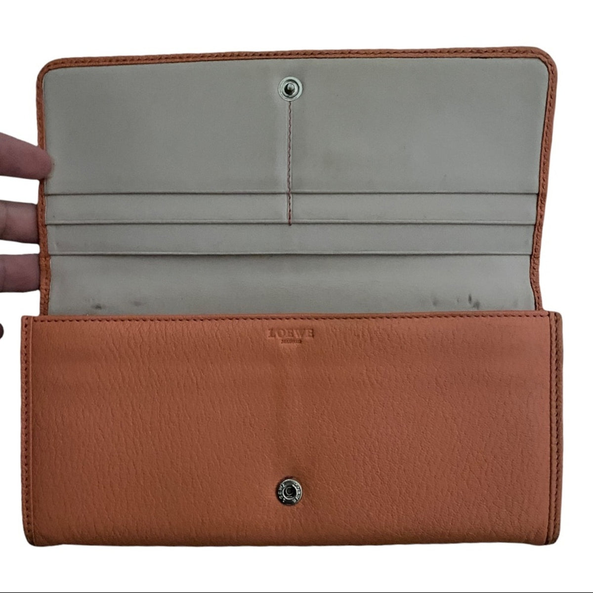 Orange wallet being held popen showing interior with pockets on a white background. 