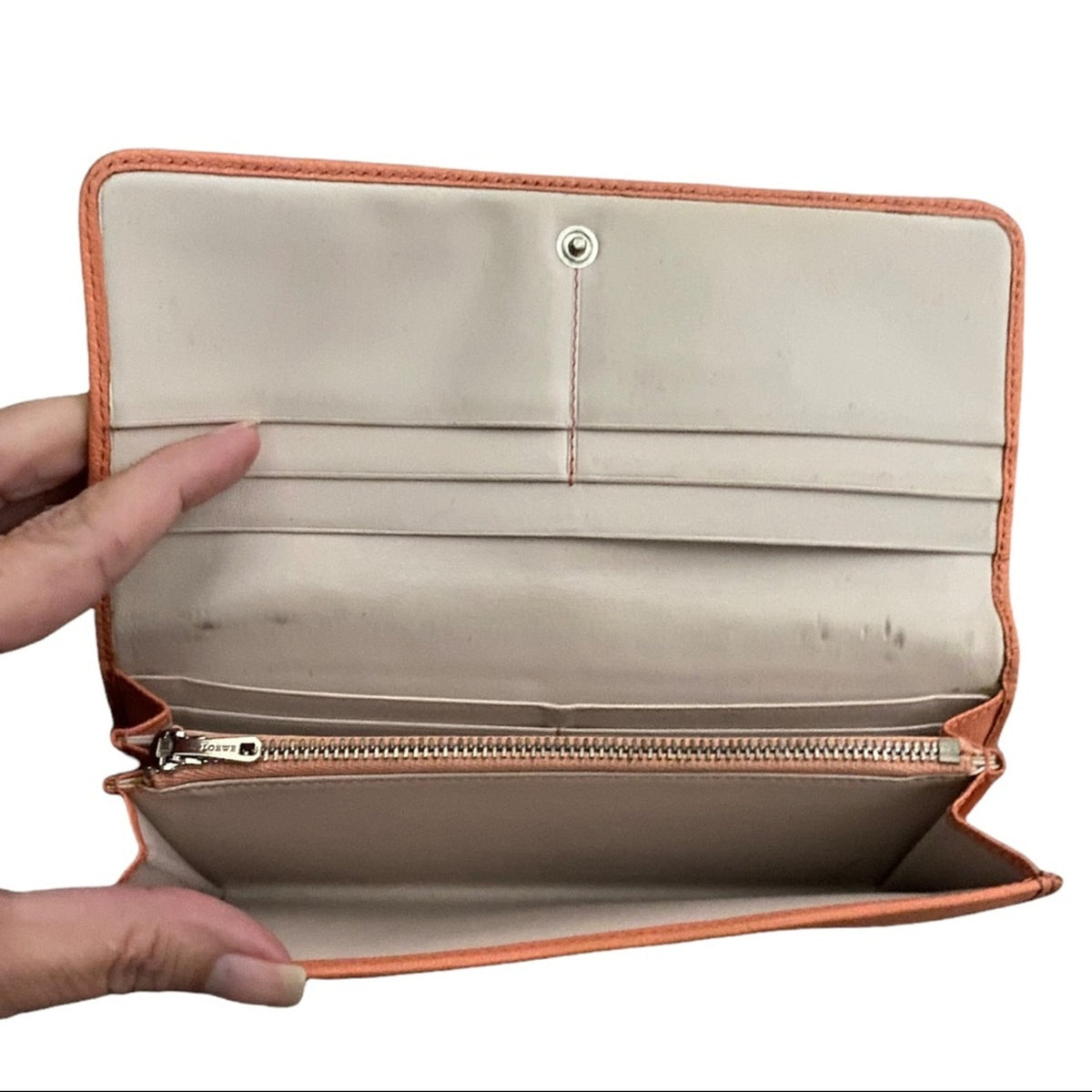 An open wallet with orange leather trim, held open by two hands against a white background.
