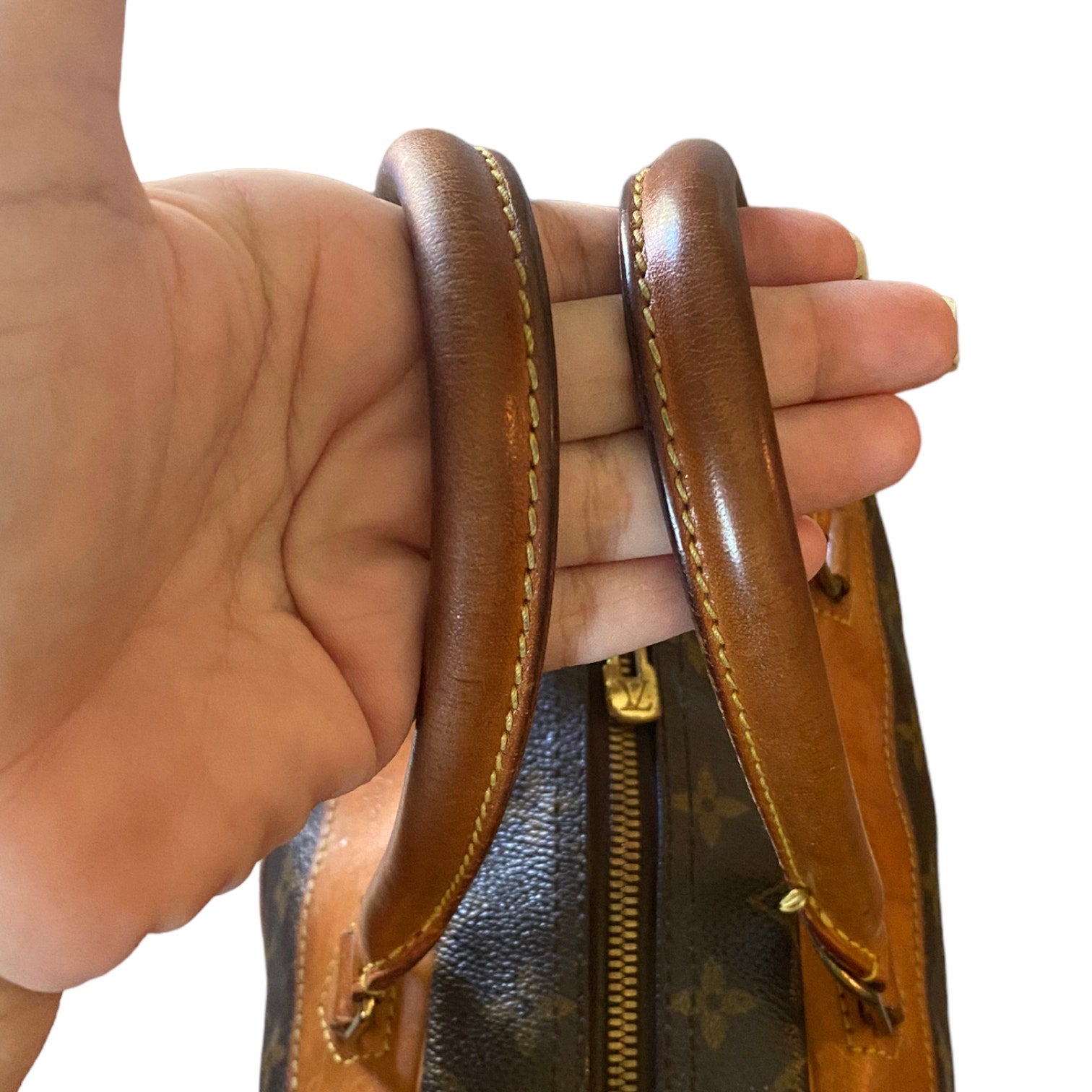 Hand holding a brown leather handle of a Louis Vuitton handbag.