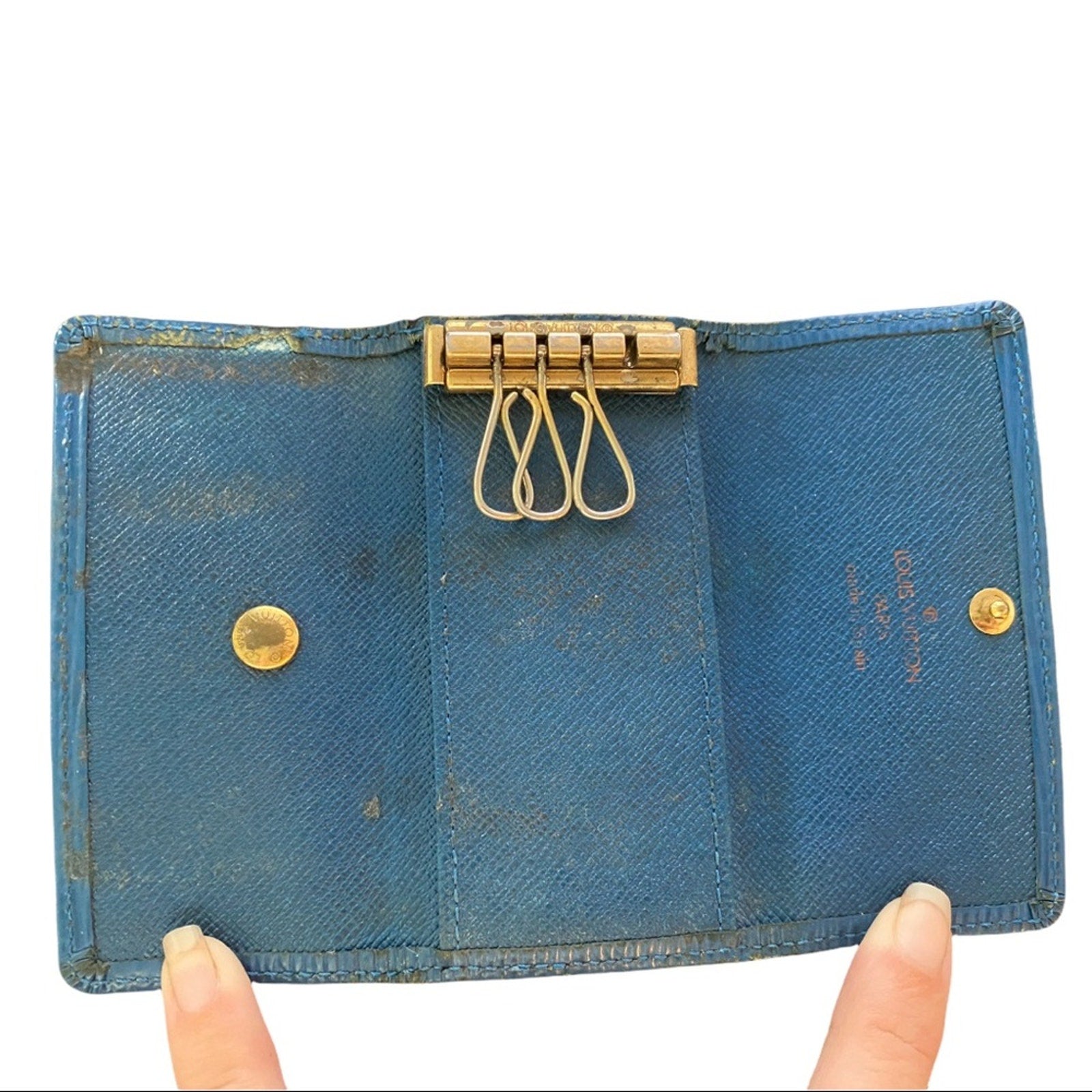 Interior of Blue wallet with gold accents held by a hand on a white background