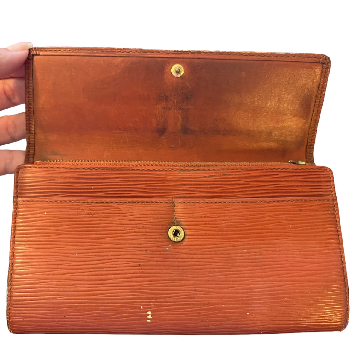 An open Louis Vuitton Epi leather wallet in a warm cognac-brown color, held open by a hand against a white background.