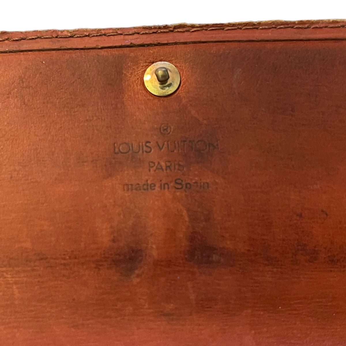 Close-up of a brown leather Louis Vuitton interior or back panel with a brass snap button and embossed 'LOUIS VUITTON PARIS made in Spain' text.