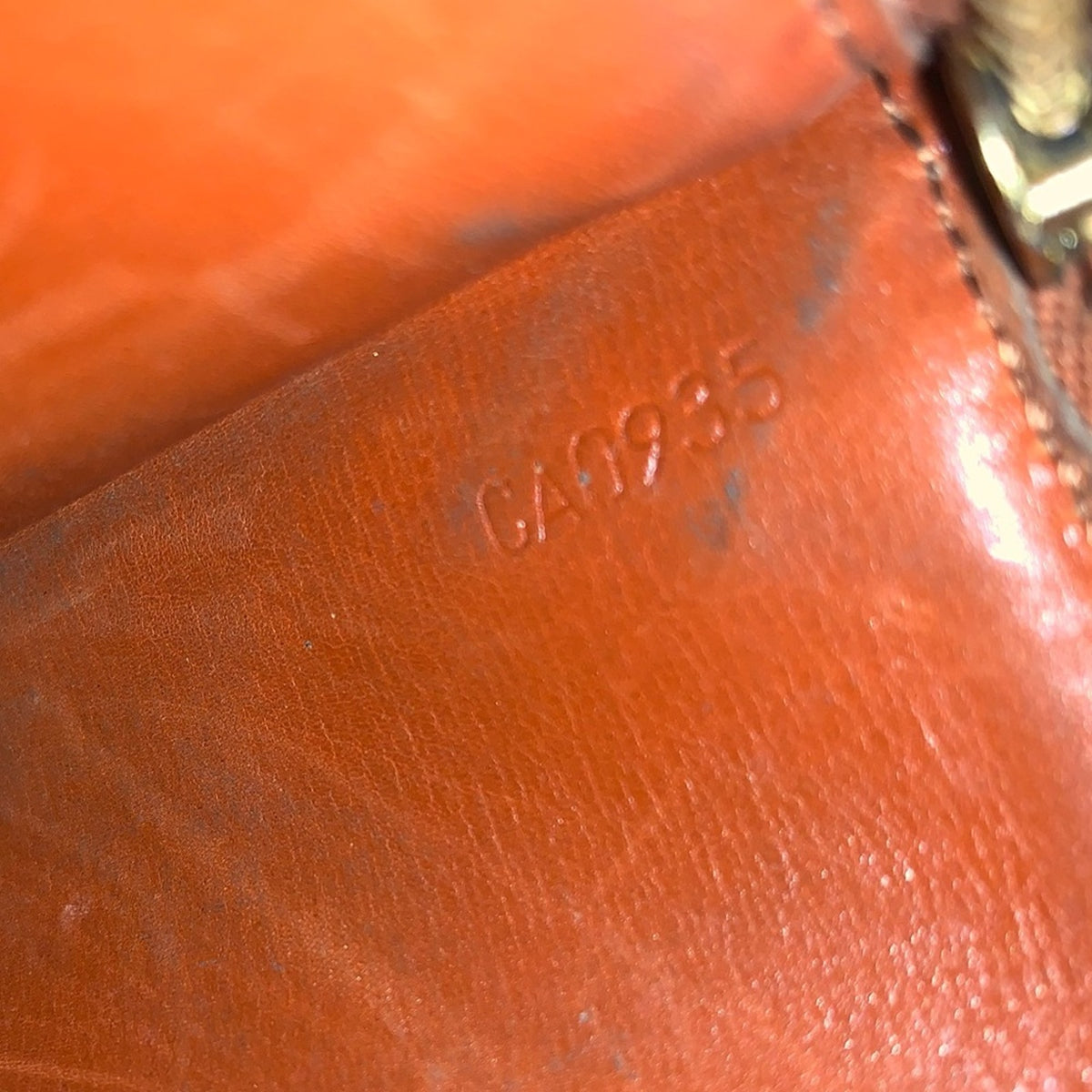 Close-up of a brown leather item showing the embossed text 'CA935' and part of a gold-toned zipper pull.