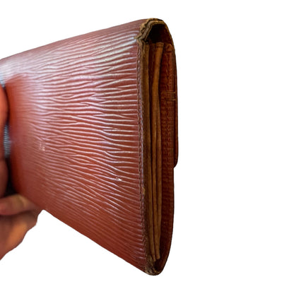 A close-up of a brown textured leather wallet being held by a hand against a plain white background.