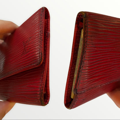 A red textured leather key wallet shown from both sides, held by hands against a plain white background. 