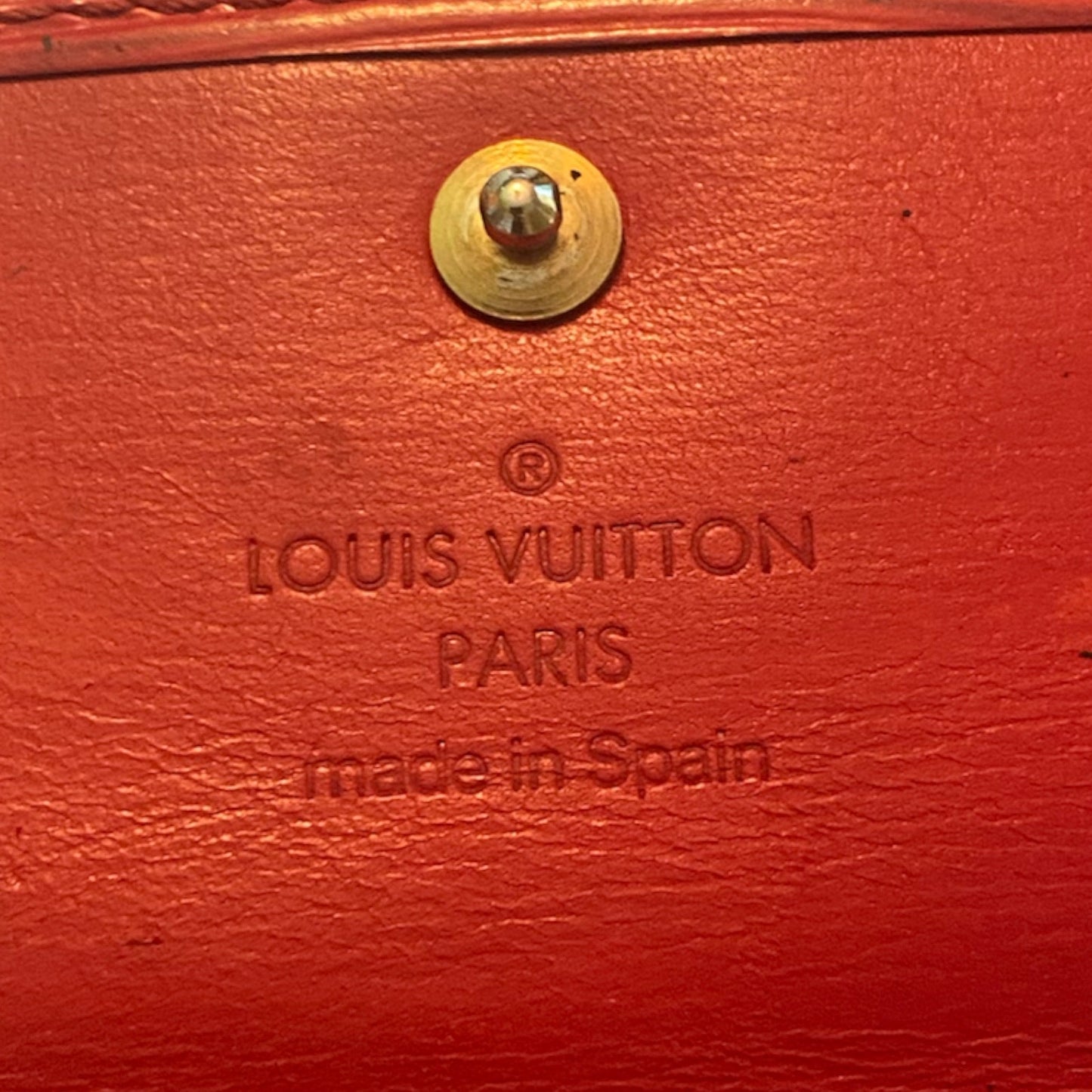 Close-up of a red Louis Vuitton leather interior or lining with a brass rivet and embossed 'LOUIS VUITTON PARIS made in Spain' text.