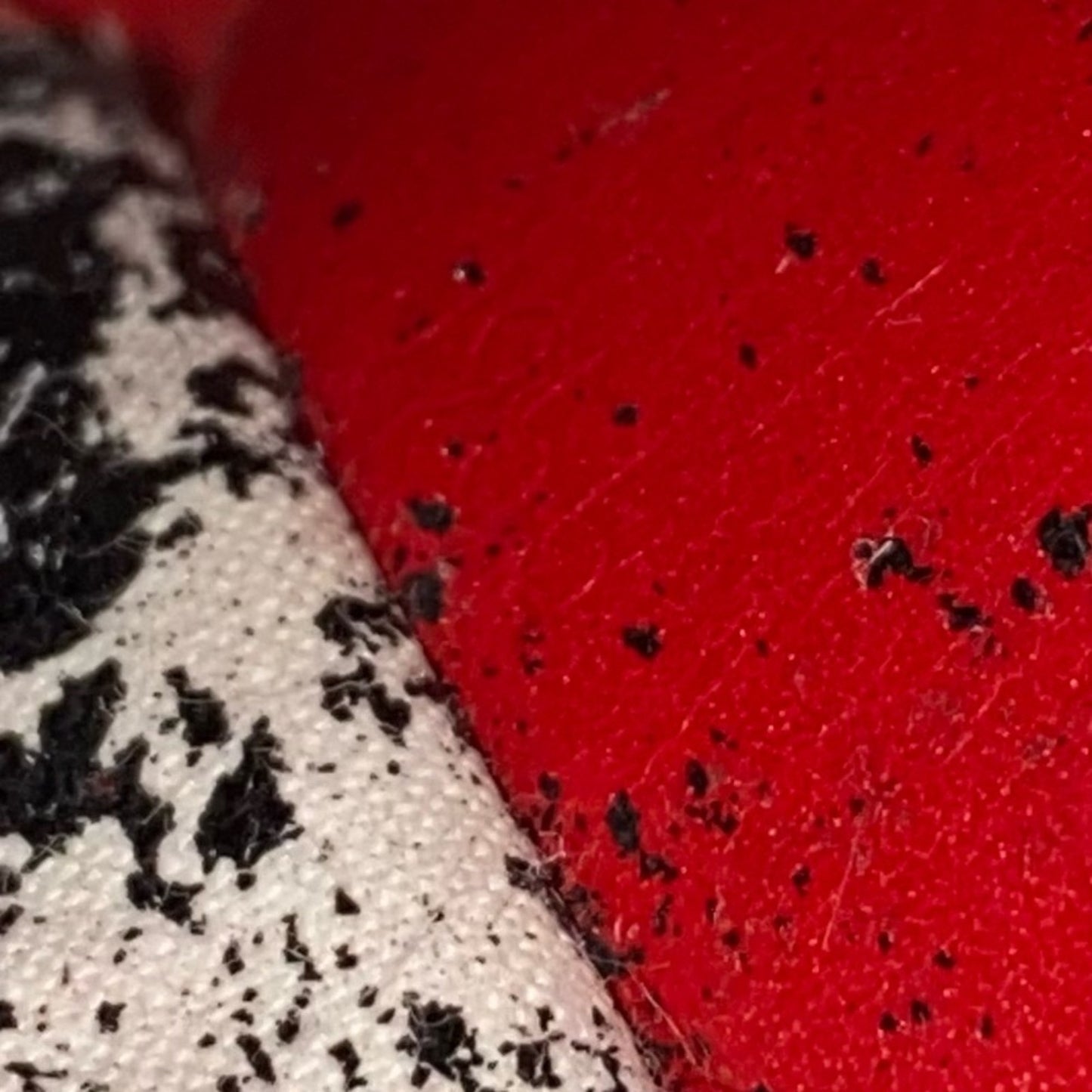 Close-up of a red textured fabric surface with scattered black peeling specks.