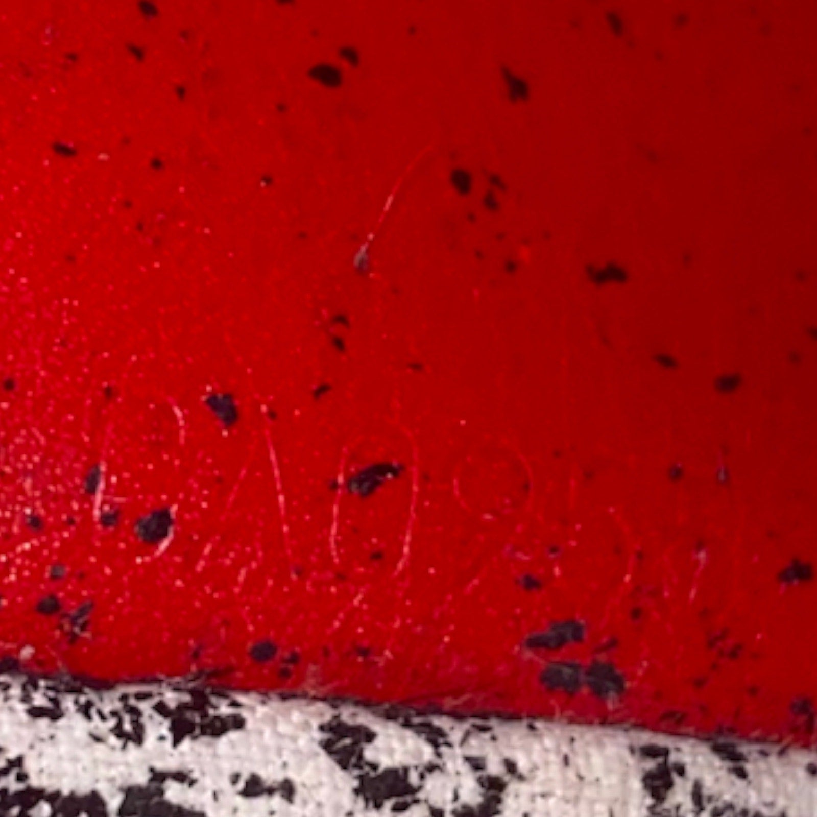 A close-up of a bright red textured surface with scattered black speckles and a date code along the bottom edge.