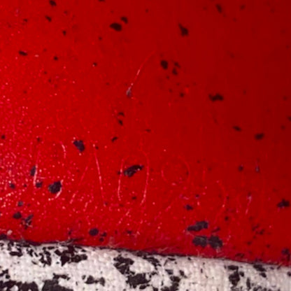 A close-up of a bright red textured surface with scattered black speckles and a date code along the bottom edge.