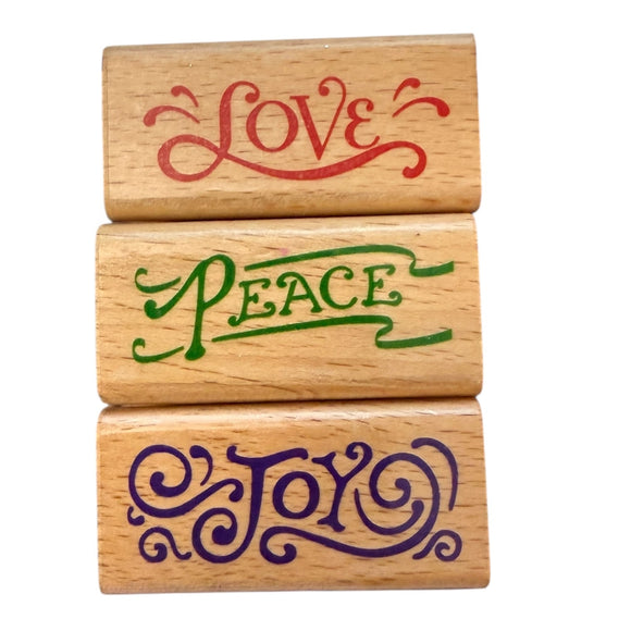 Three wooden stamps with 'Love', 'Peace', and 'Joy' engraved on them.