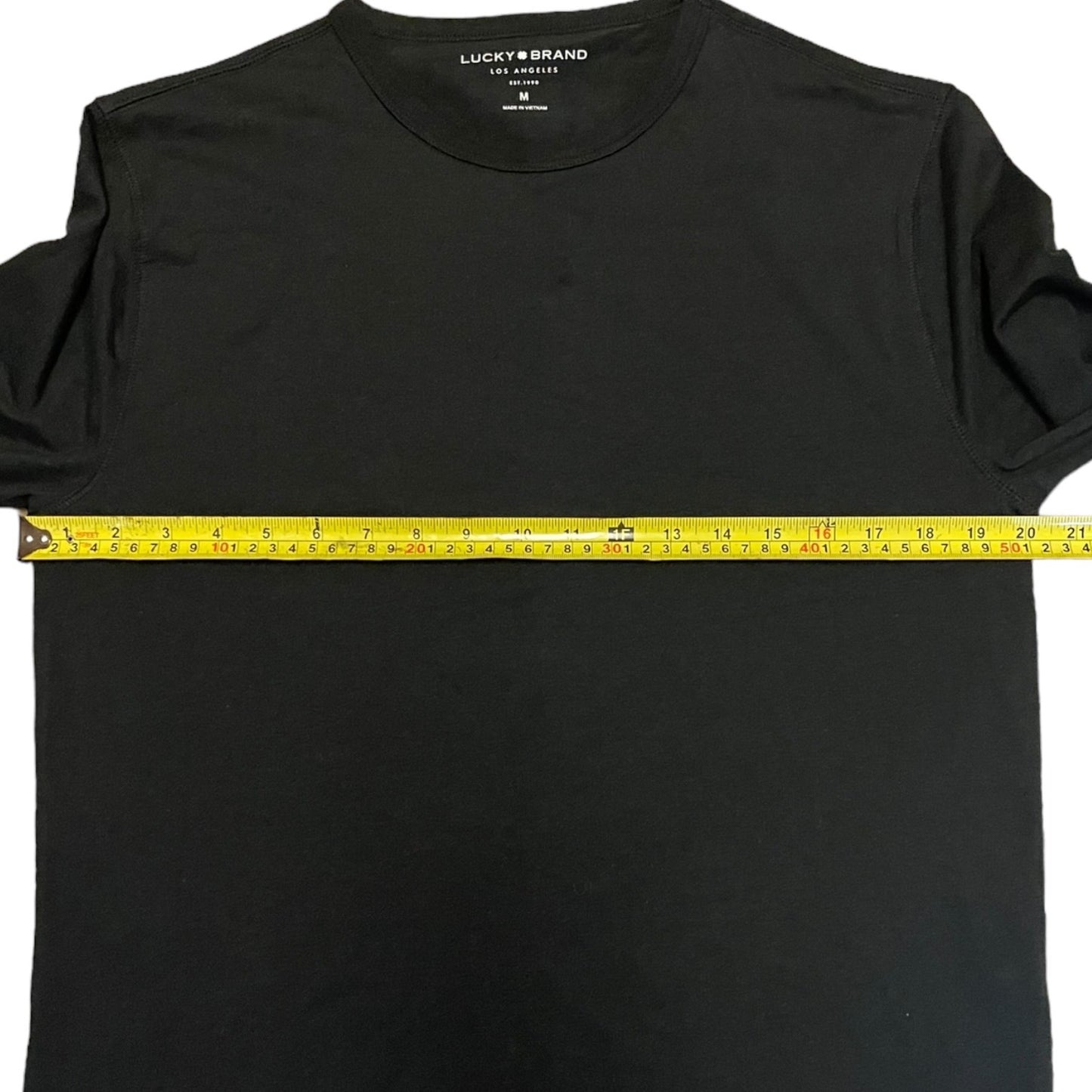 Black shirt with a measuring tape across it, displaying the brand 'Lucky Brand'.