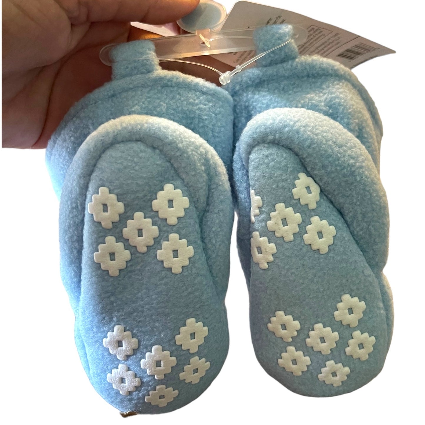 Pair of blue baby shoes with white floral patterns held by a hand against a white background.