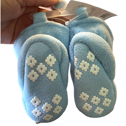 Pair of blue baby shoes with white floral patterns held by a hand against a white background.