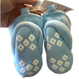 Pair of blue baby shoes with white floral patterns held by a hand against a white background.