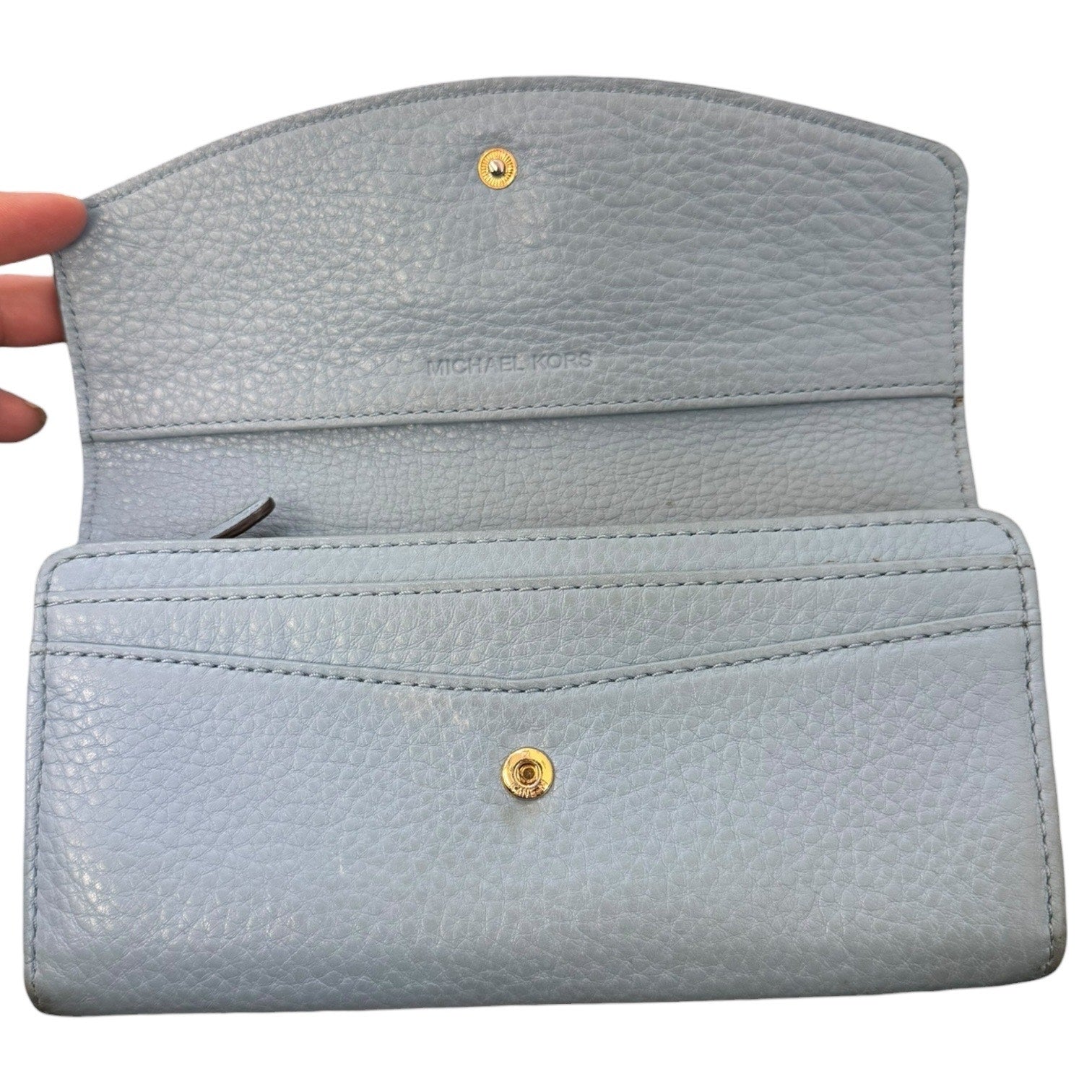 Interior of Light blue wallet with gold buttons held by a hand on a white background