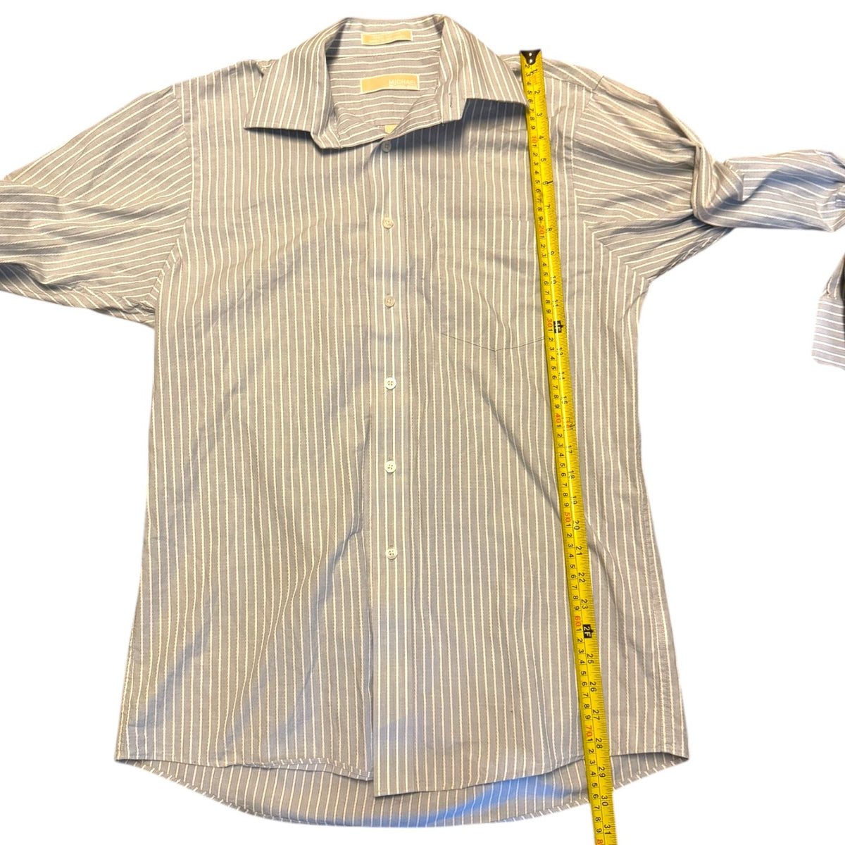 A men's long-sleeve button-up shirt with thin vertical stripes in blue and white, laid flat on a white background with a yellow measuring tape standing vertically next to it for size reference.