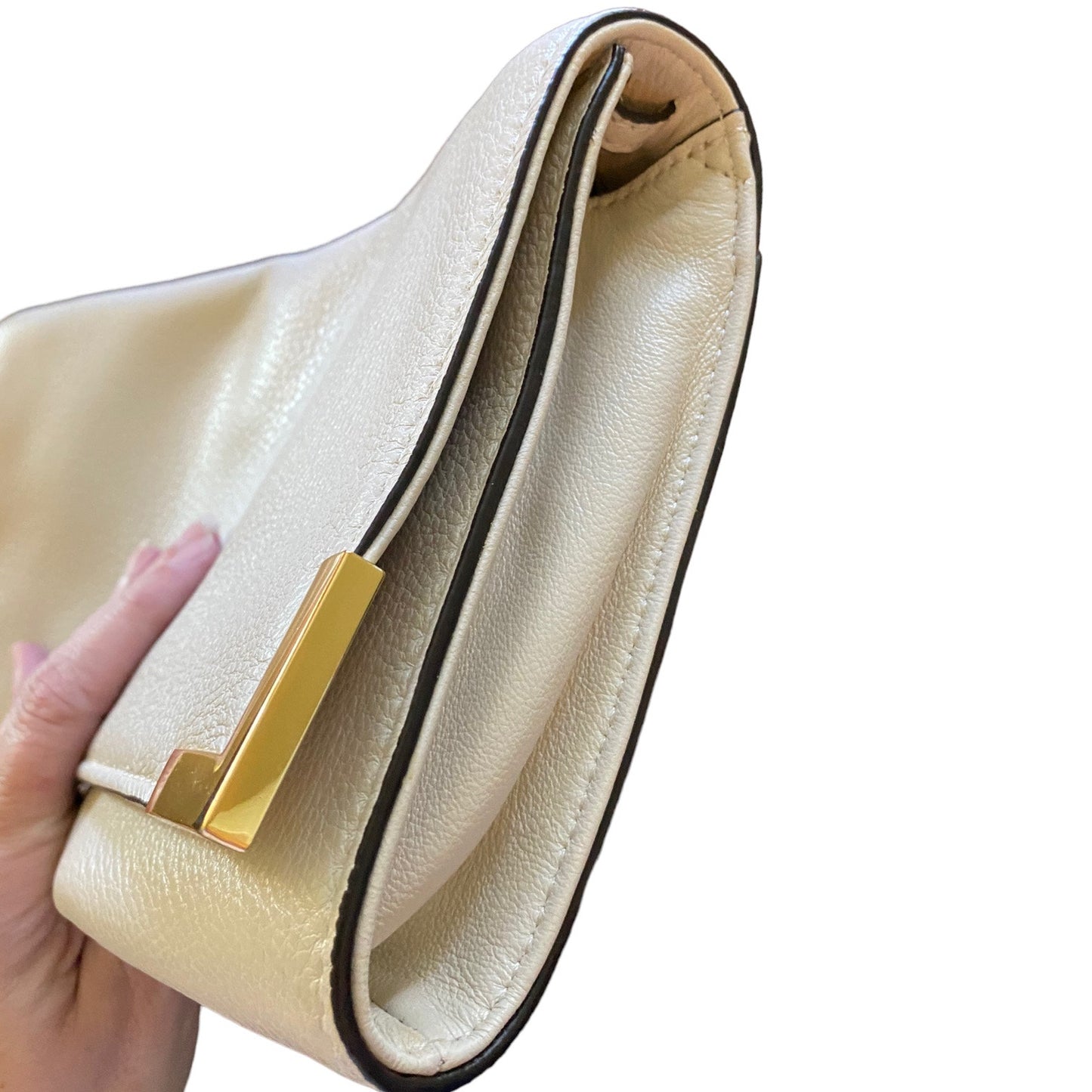 Side view of bag with a gold clasp held by a hand on a white background
