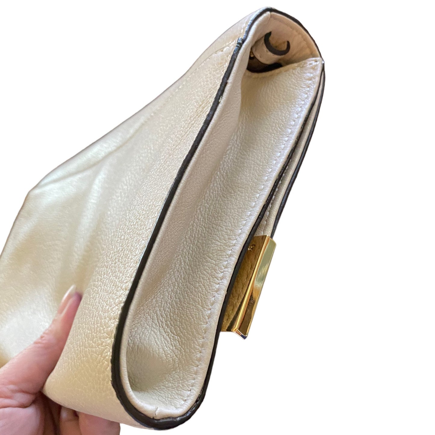 A close-up of a pebbled leather clutch side view handbag being held by a hand, featuring a gold-tone metal clasp and dark brown trim.