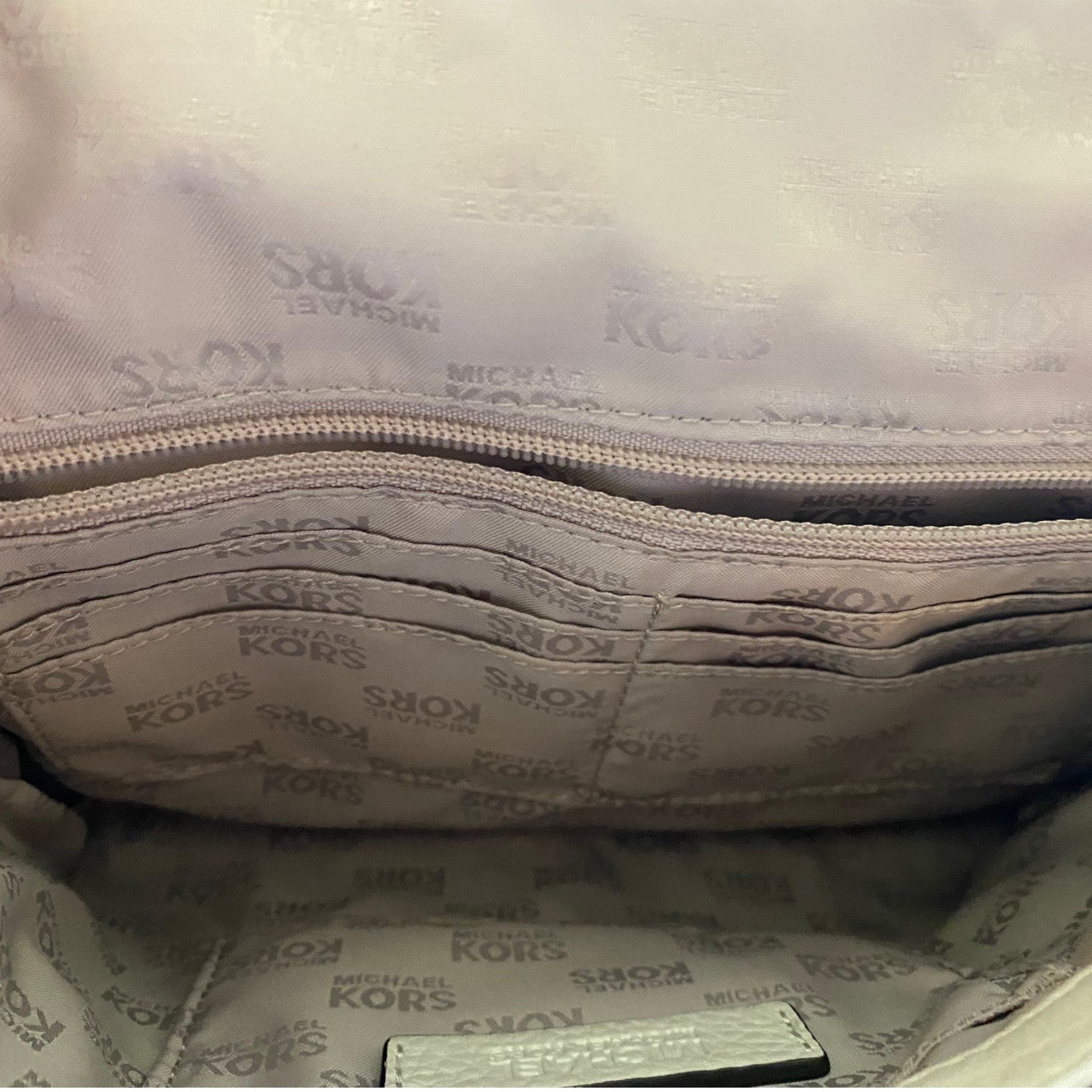 Close-up interior view of a Michael Kors handbag showing the branded interior lining with a repeating MICHAEL KORS pattern and a zippered compartment.