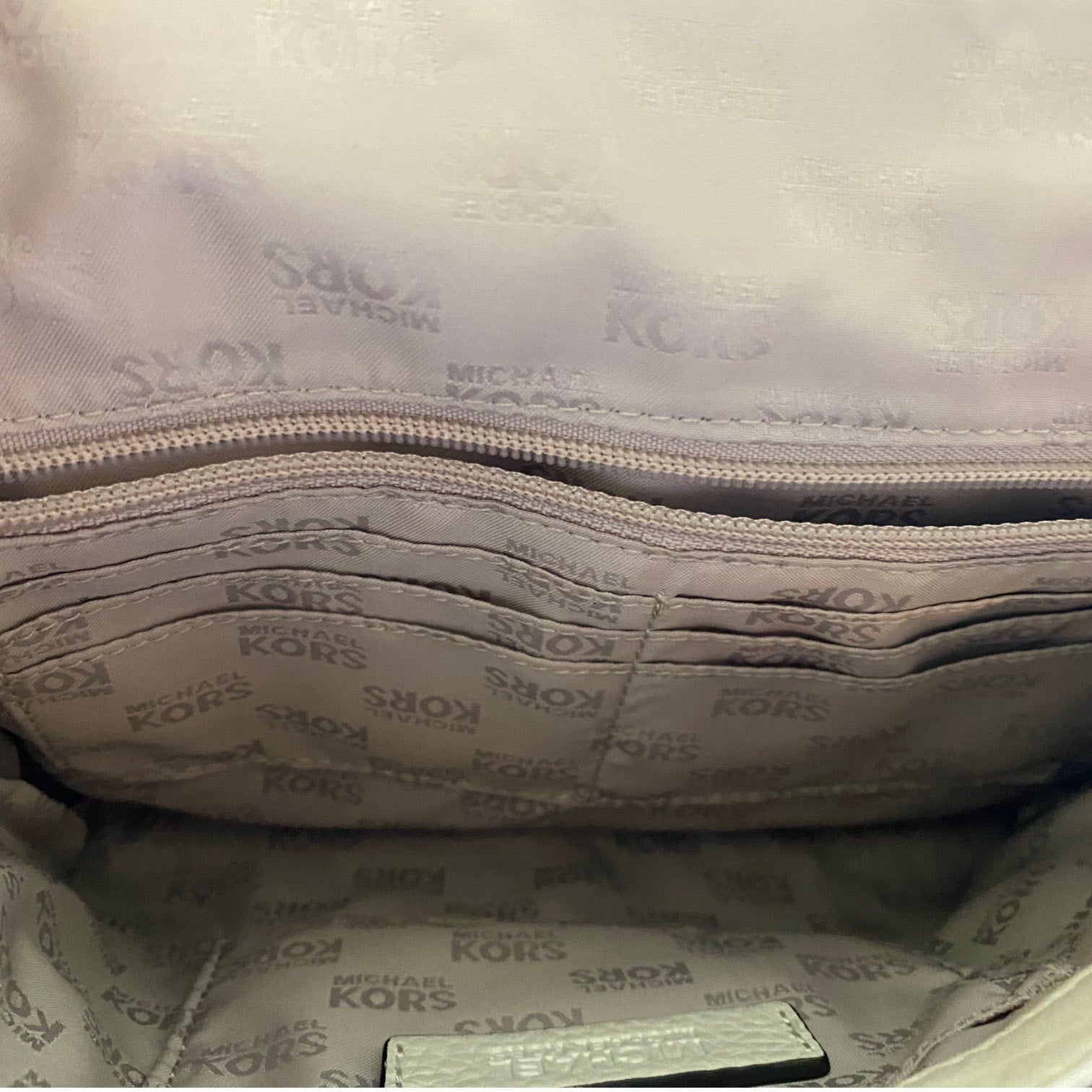 Close-up interior view of a Michael Kors handbag showing the branded interior lining with a repeating MICHAEL KORS pattern and a zippered compartment.