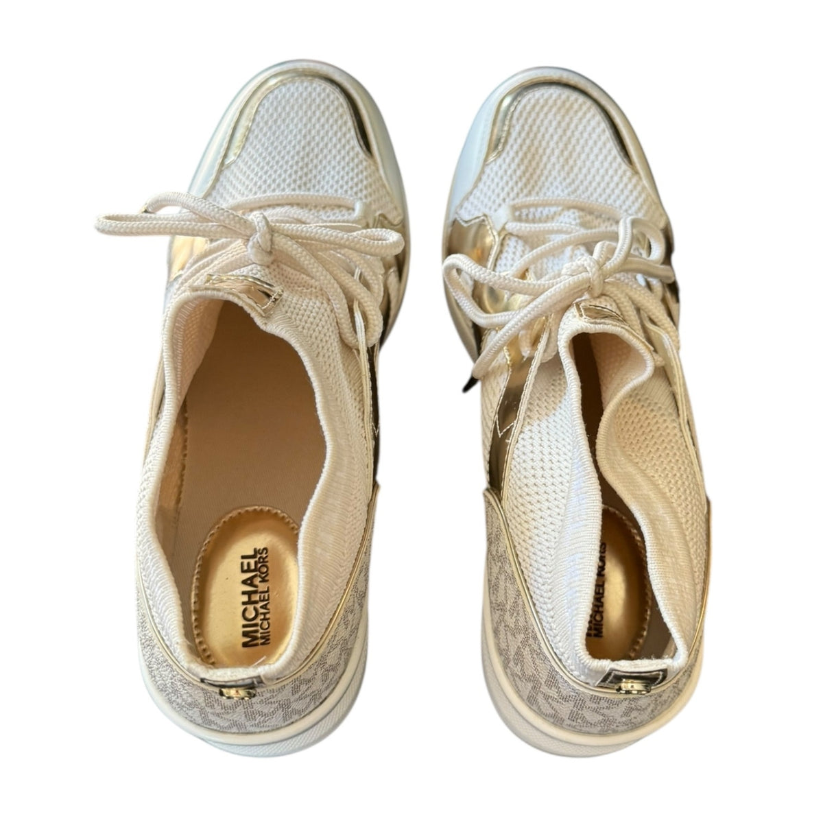 A pair of Michael Kors sneakers shown from the top, featuring a white mesh upper, gold metallic side panels, and a signature monogram pattern on the heel.