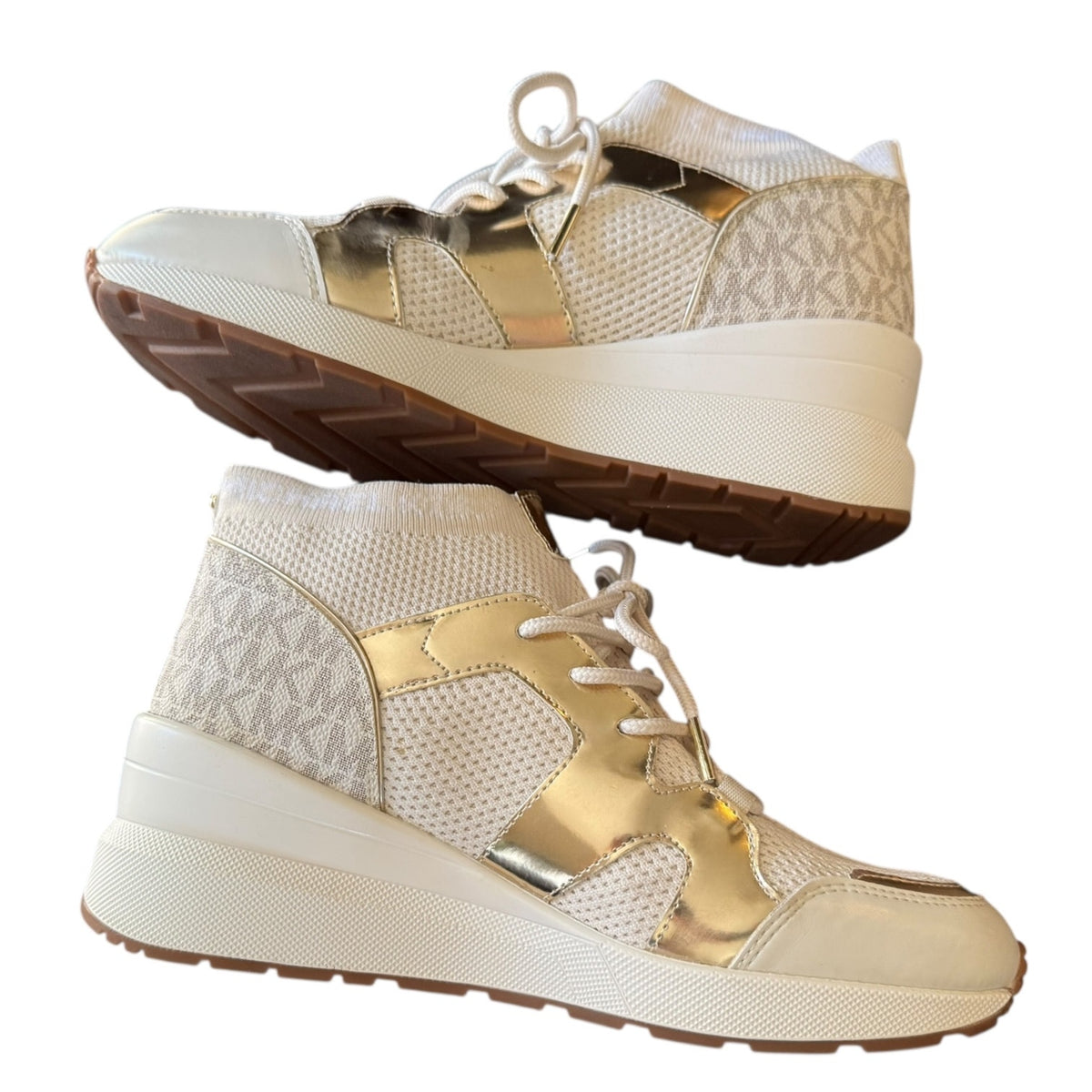 A pair of high-top sneakers shown from the side and bottom angles against a plain white background. The shoes feature a white mesh with metallic gold panels.