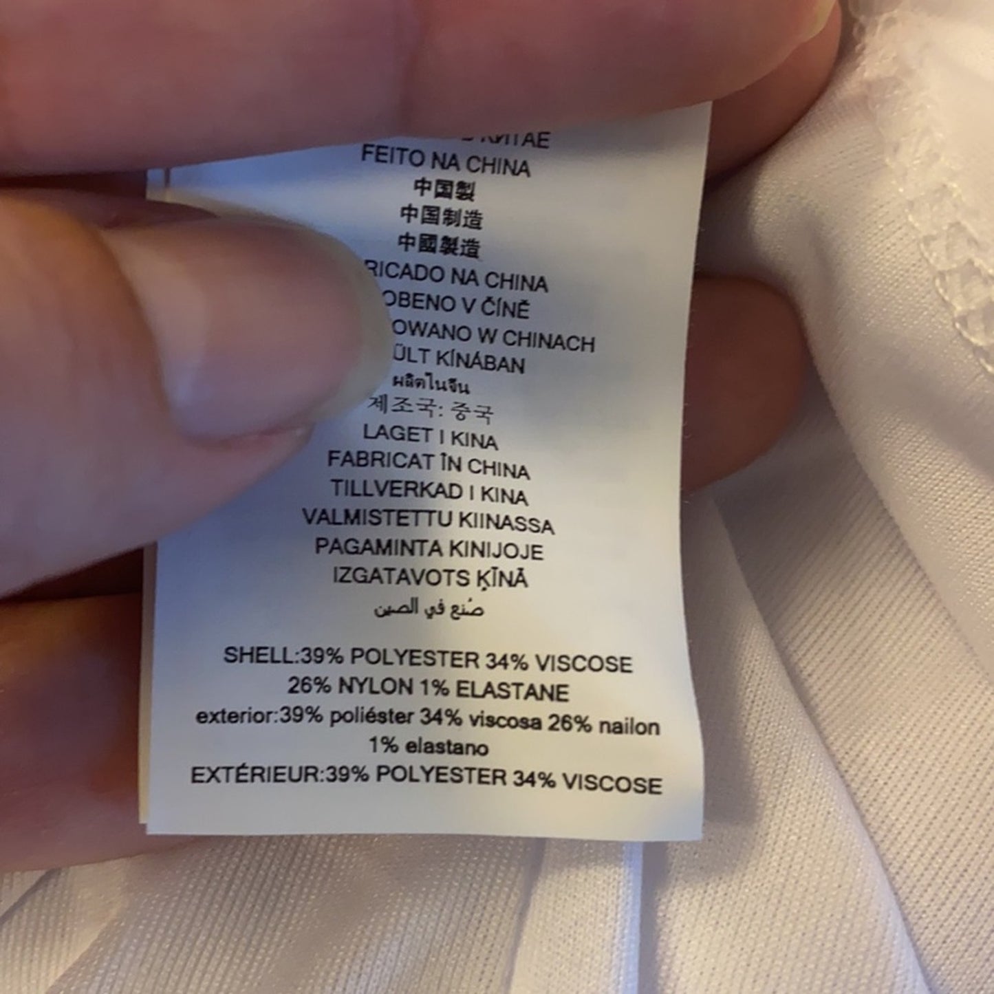 Clothing label with text held by a hand against a beige fabric background