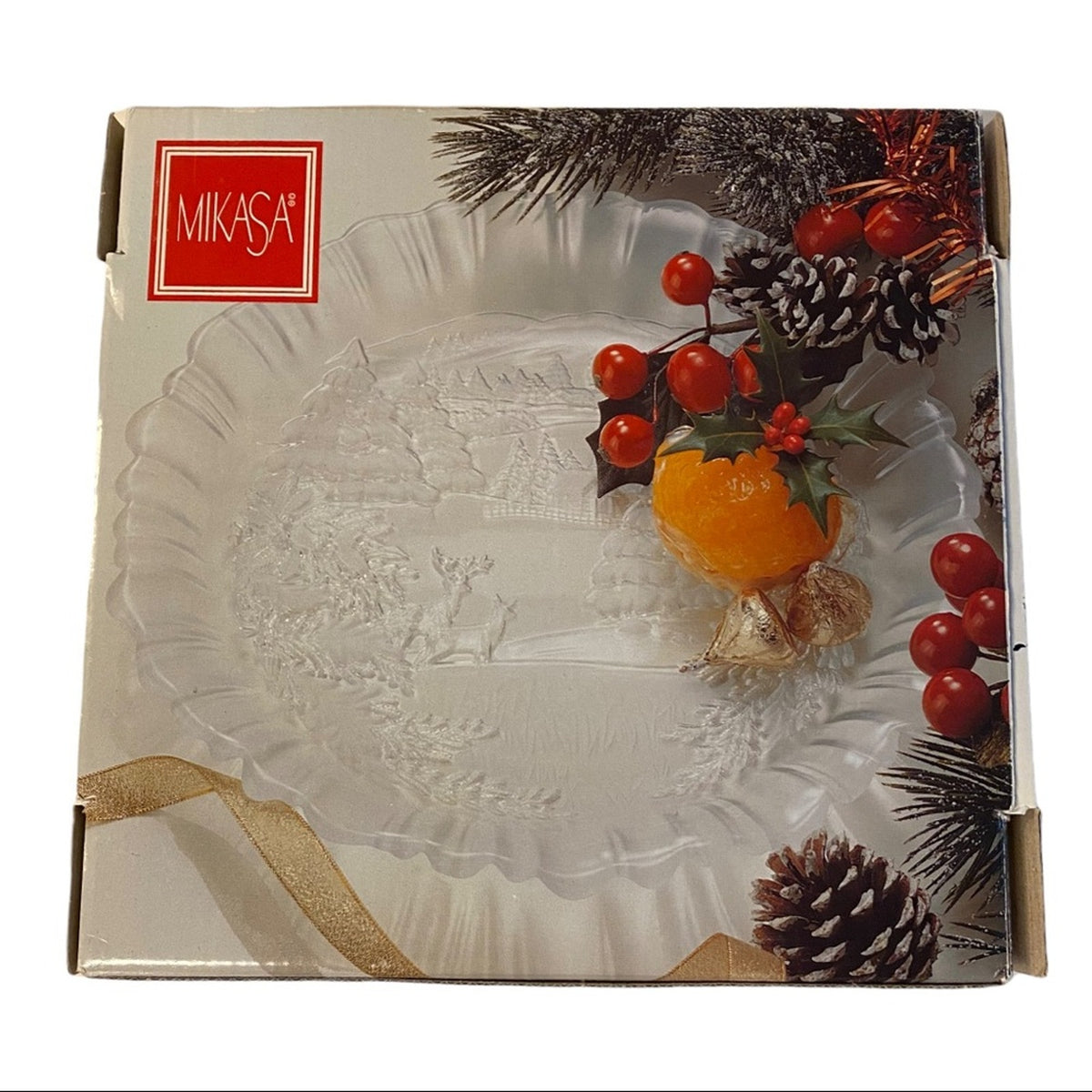 Mikasa Christmas-themed glass platter in its original retail packaging, decorated with festive illustrations of pine branches, red berries, holly, and a gold ribbon.
